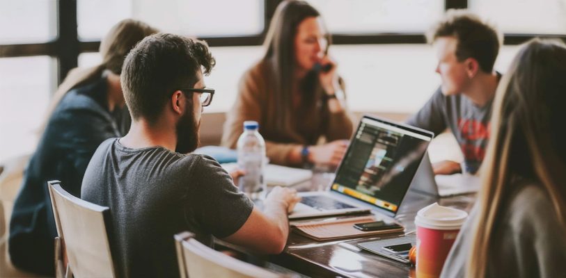 a group of people sitting at a table looking at a laptop